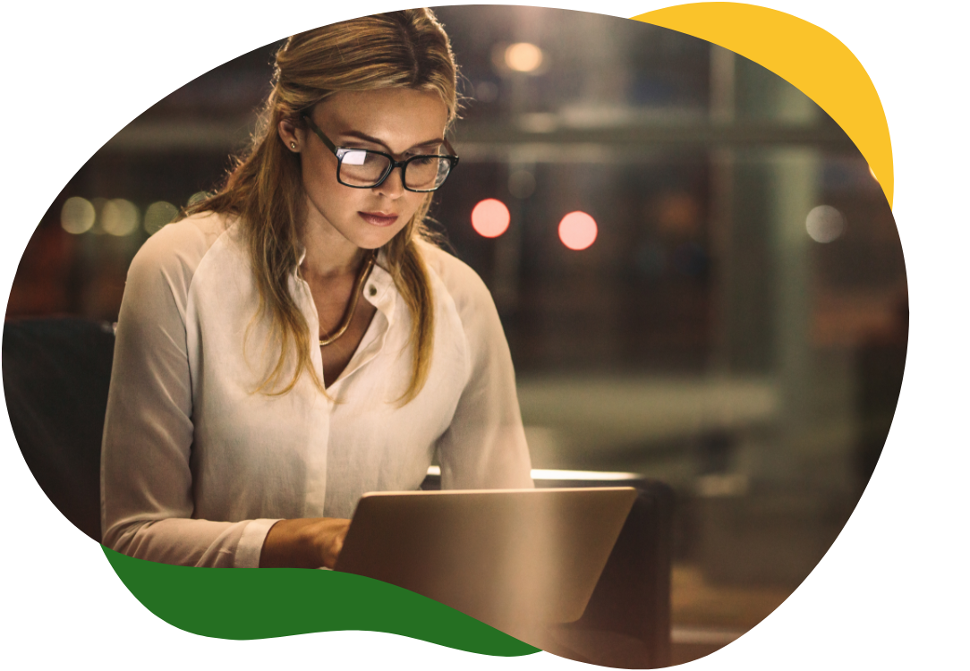 Mlada žena s naočalama i vezanom kosom u poslovnoj odjeći i dalje radi na laptopu u uredu kasno navečer