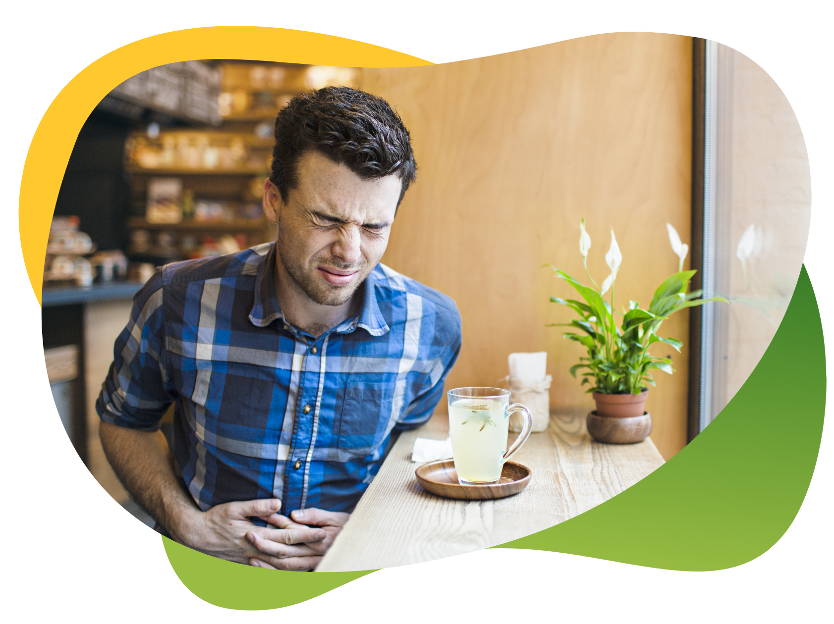 Mladić sjedi pored prozora u kafiću i drži se za trbuh s bolnim izrazom na licu - čaša s pićem ispred njega je prazna