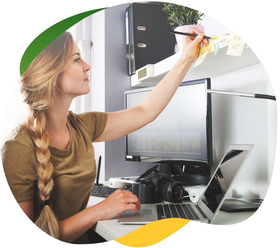 Mlada žena s plavom pletenicom sjedi za svojim radnim stolom i piše zabilješke na post-it papiriće.